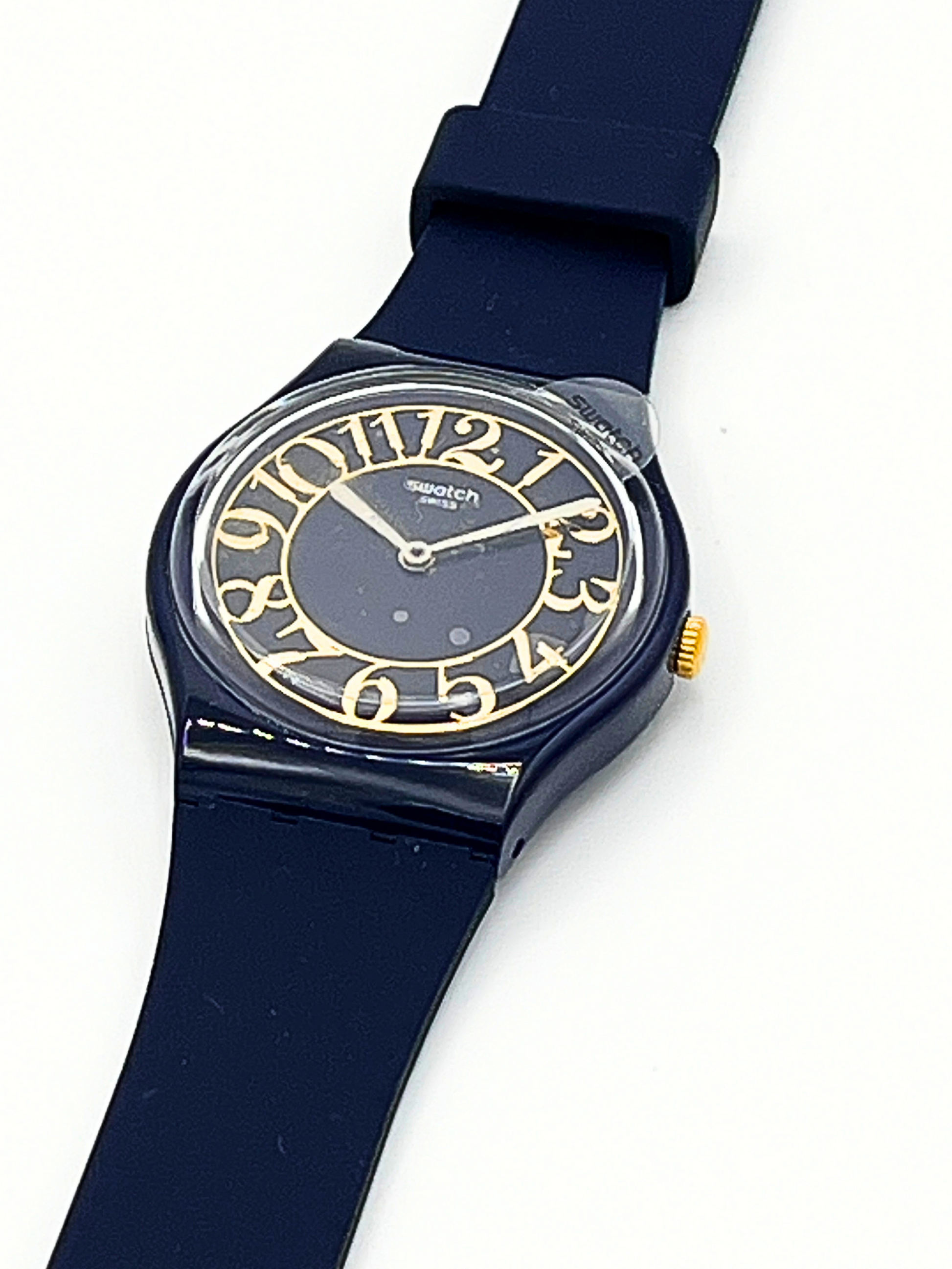 A vintage Swatch wristwatch featuring a dark navy blue silicone strap, a matching dark blue dial, and gold-tone Arabic numerals and crown details, shown on a plain white background.