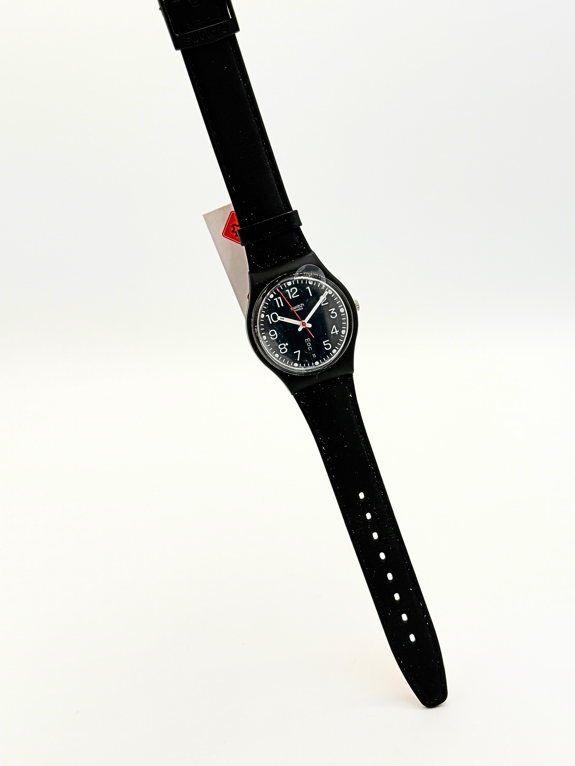 A black Swatch wristwatch with a black strap and black dial, held by a hand against a plain white background.