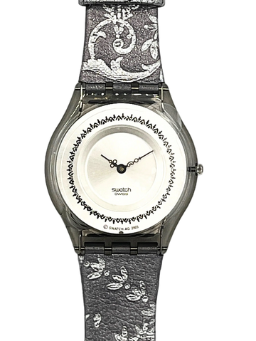 Swatch London analog watch with a textured gray and white patterned strap, a silver-toned case, and a white dial featuring a black decorative border.