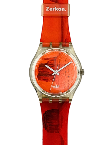 A wristwatch with a bright orange-red silicone strap and matching dial, featuring a silver-tone round case and Swatch branding on the dial and Zerkon on the buckle.