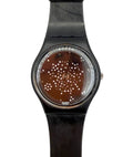 A Swatch wristwatch with a black strap and case, featuring a brown dial decorated with a pattern of small white dots.