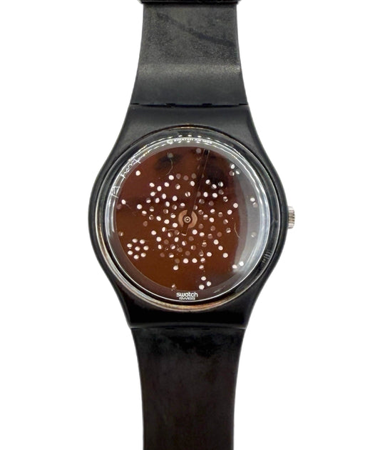 A Swatch wristwatch with a black strap and case, featuring a brown dial decorated with a pattern of small white dots.