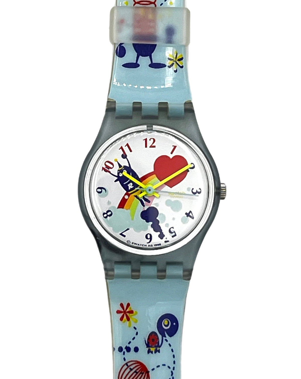 A Swatch wristwatch featuring a light blue silicone strap and case with a whimsical multicolor cartoon design, including a red heart, blue characters, and yellow stars on a white dial.