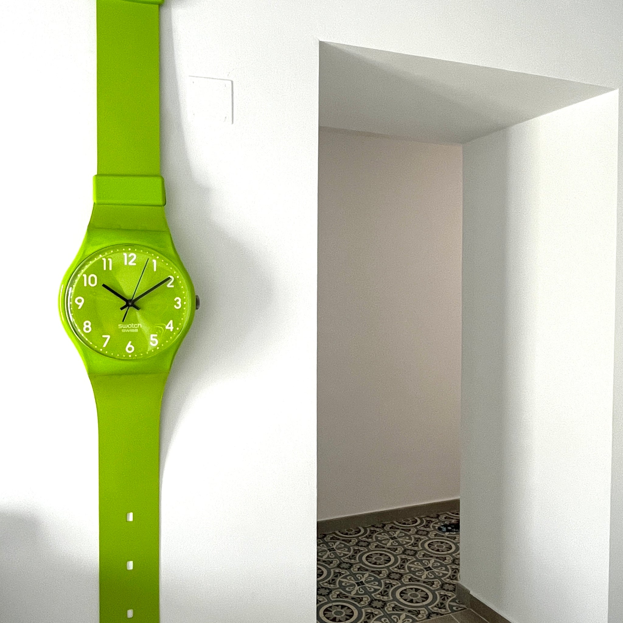 Green watch on a white wall with a doorway in the background