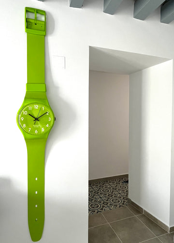 Green watch on a white wall with a doorway in the background