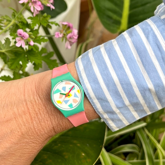 A Swatch Gent watch with an orange plastic band and petrol colored dial, featuring orange hands.