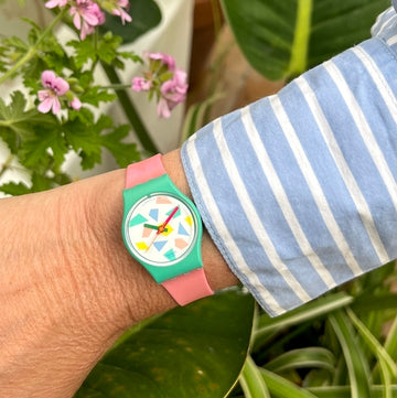 A Swatch Gent watch with an orange plastic band and petrol colored dial, featuring orange hands.