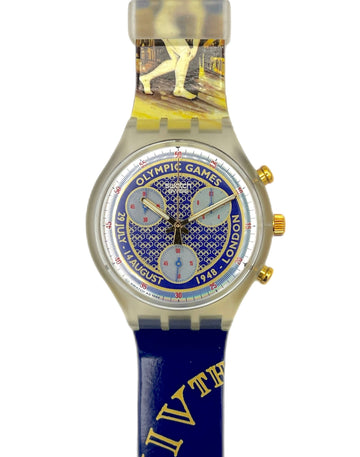 A Swatch watch featuring a blue silicone strap with gold Roman numerals and a graphic of a golfer, a blue dial with 'Olympic Games 1948 London' text, and a clear plastic buckle.
