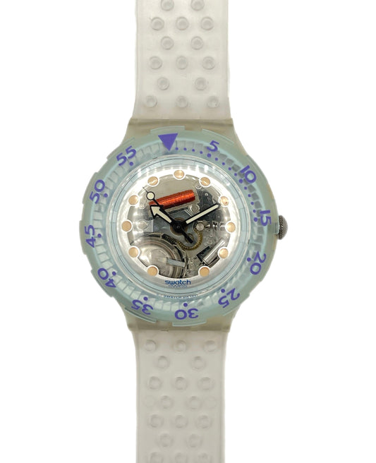 A Swatch wristwatch with a translucent light blue-green bezel, a white textured silicone strap, and a visible mechanical movement inside the clear dial.