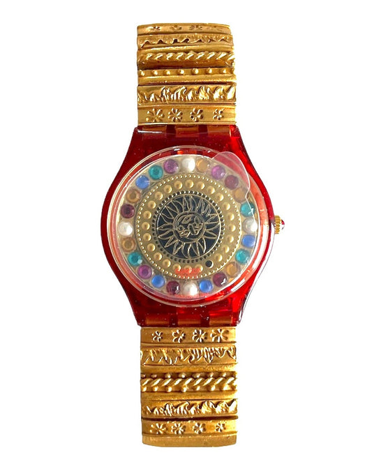 Decorative watch with red face, gold casing, and colorful gemstones on a white background
