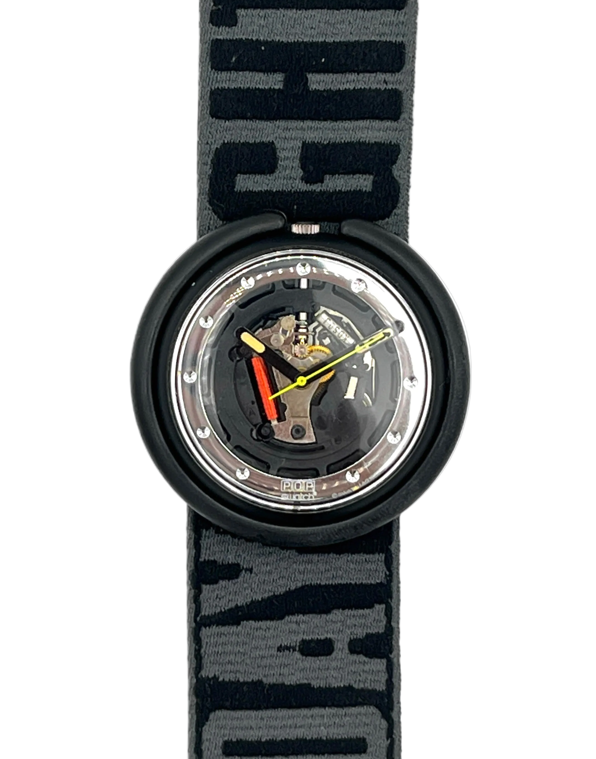 A Swatch wristwatch with a black circular case and a patterned gray and black fabric strap. The watch face is transparent, showing the internal mechanical movement with gold, silver, and red details.