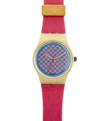A Swatch wristwatch featuring a bright pink strap, a gold-tone case, and a blue dial with a pink checkerboard pattern.