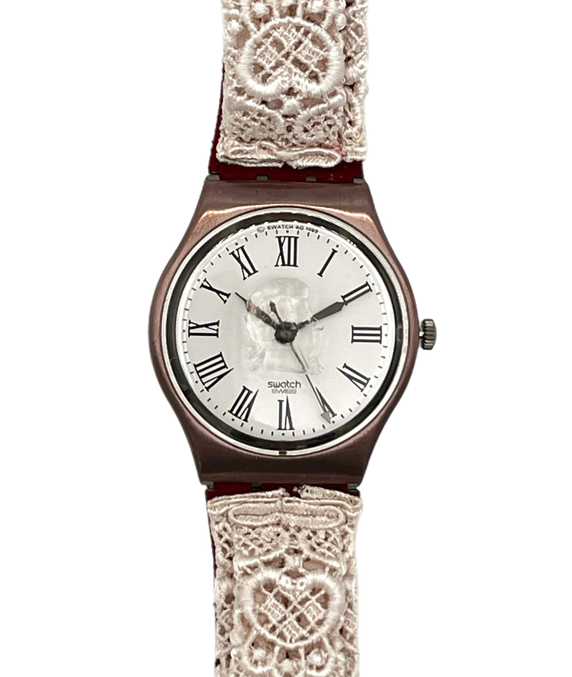 A vintage-style wristwatch with a round rose gold-toned case, a white dial with black Roman numerals, and a decorative off-white lace strap, shown against a plain white background.