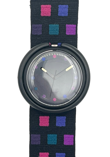 A wristwatch with a round black bezel and a dark strap featuring a colorful geometric pattern of pink, purple, and blue squares, shown against a plain white background.