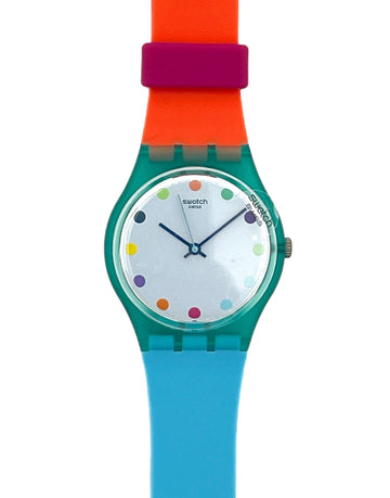 A Swatch wristwatch with a translucent teal case, a white dial decorated with colorful polka dots, and a vibrant color-blocked strap in orange, magenta, and light blue.