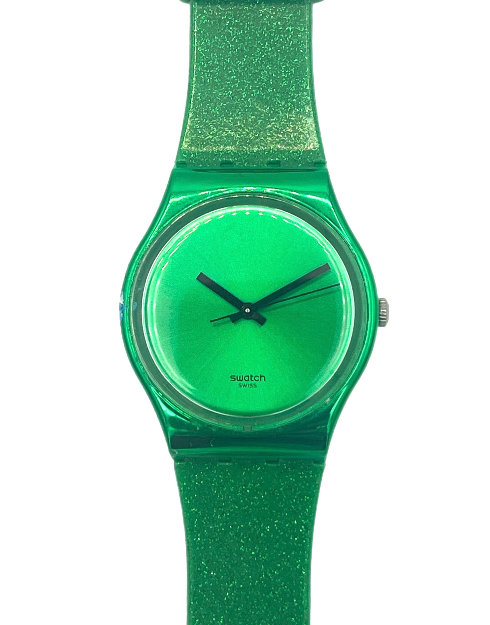 A Swatch wristwatch featuring a translucent green case, matching green dial, and a glittery green strap, shown against a plain white background.