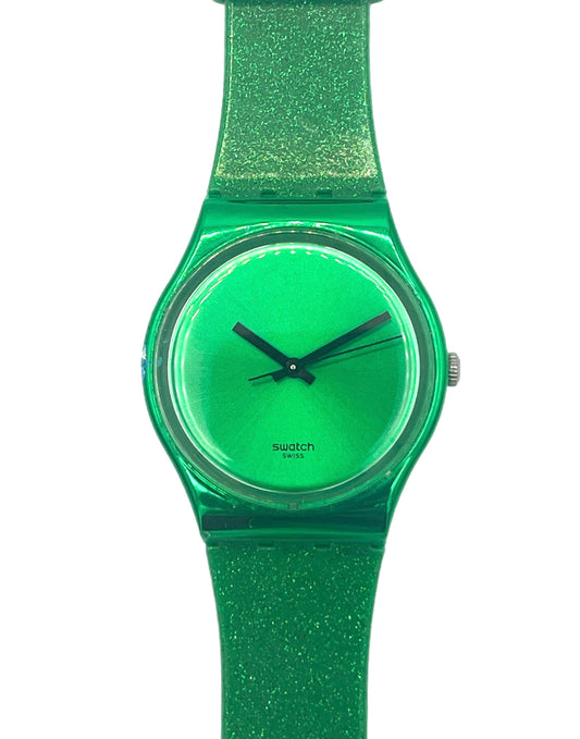 A Swatch wristwatch featuring a translucent green case, matching green dial, and a glittery green strap, shown against a plain white background.