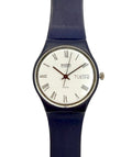 A Swatch wristwatch with a dark blue strap, a silver-tone case, and a white dial featuring black Roman numerals and a day window.