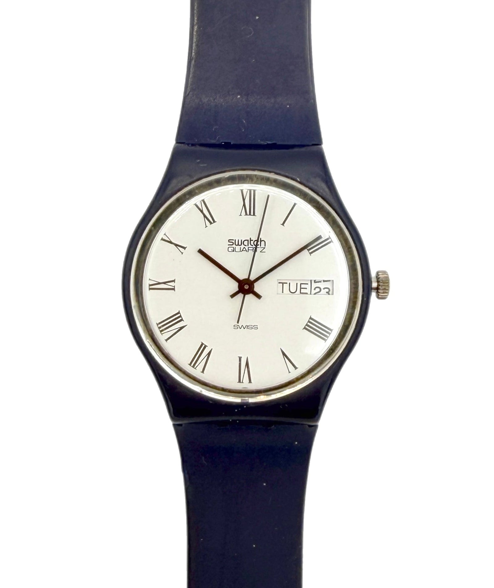 A Swatch wristwatch with a dark blue strap, a silver-tone case, and a white dial featuring black Roman numerals and a day window.