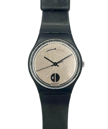 A Swatch watch with a black strap and case, featuring a textured beige dial with black hands and a black logo at the bottom.