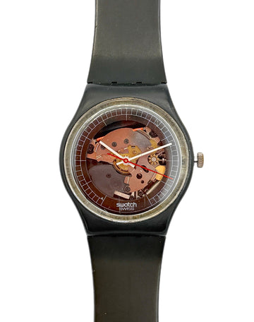 Swatch wristwatch with a black strap and case, featuring a transparent dial that reveals a copper-toned mechanical movement inside, shown against a plain white background.