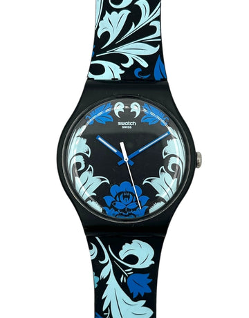 Swatch watch with a black case and a strap featuring a blue and light blue floral damask pattern, shown against a plain white background.