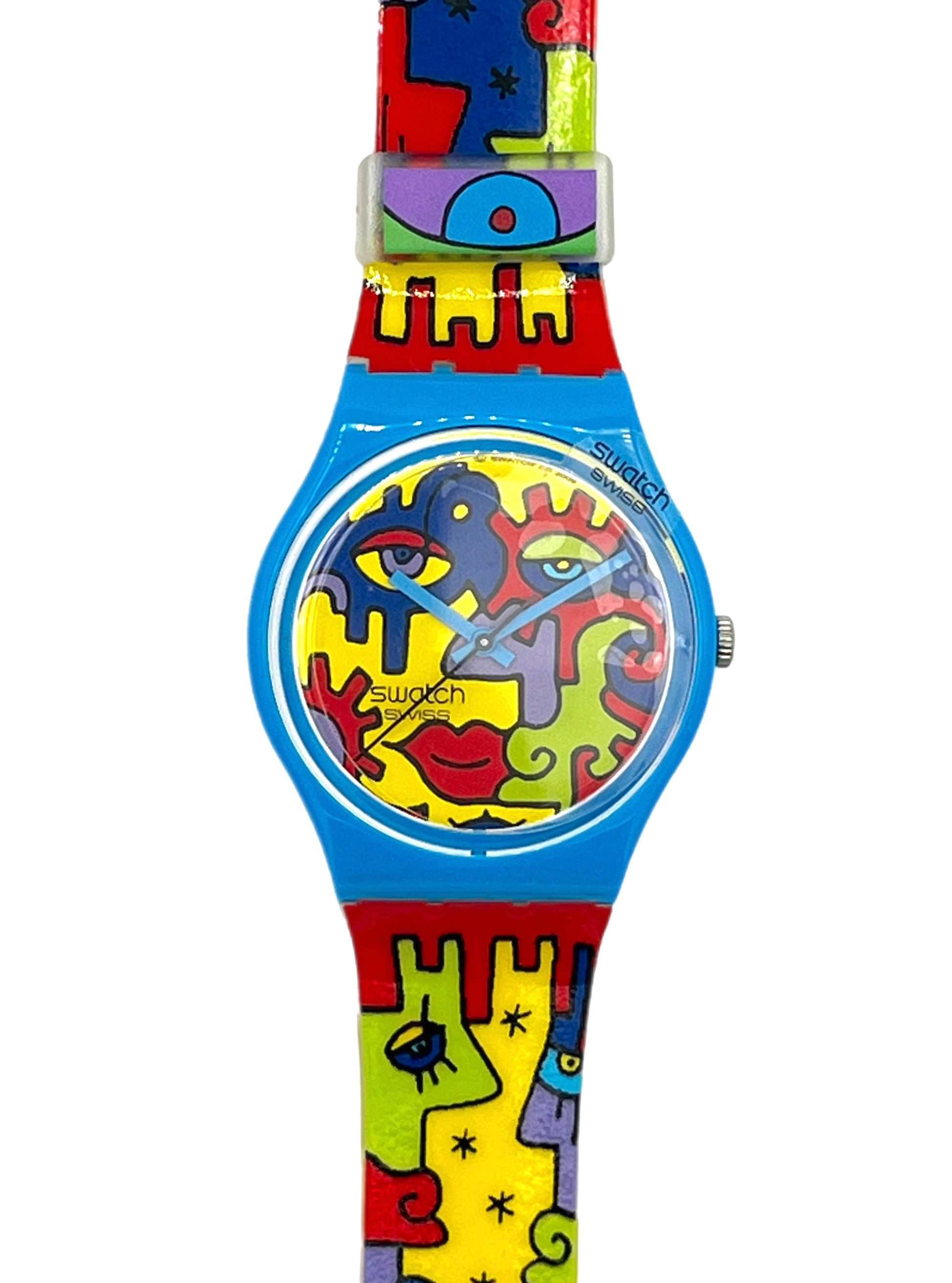 Swatch wristwatch with a bright blue case and a colorful abstract puzzle-piece strap featuring red, yellow, green, and purple shapes on a white background.
