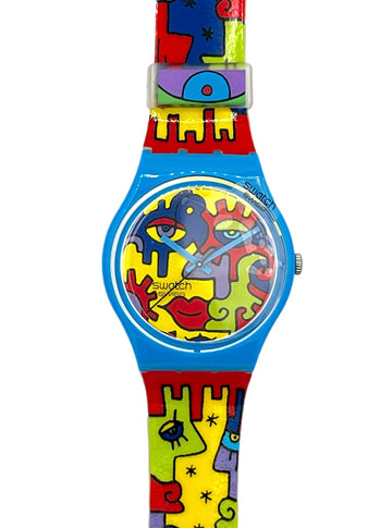 Swatch wristwatch with a bright blue case and a colorful abstract puzzle-piece strap featuring red, yellow, green, and purple shapes on a white background.