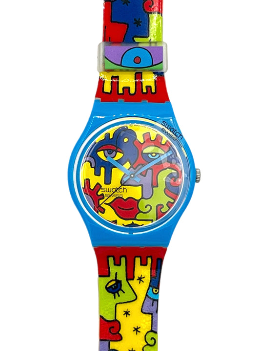 Swatch wristwatch with a bright blue case and a colorful abstract puzzle-piece strap featuring red, yellow, green, and purple shapes on a white background.