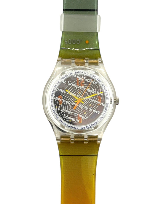 A Swatch wristwatch with a translucent olive green and yellow-green strap, a clear case, and a detailed multicolor sun face dial.