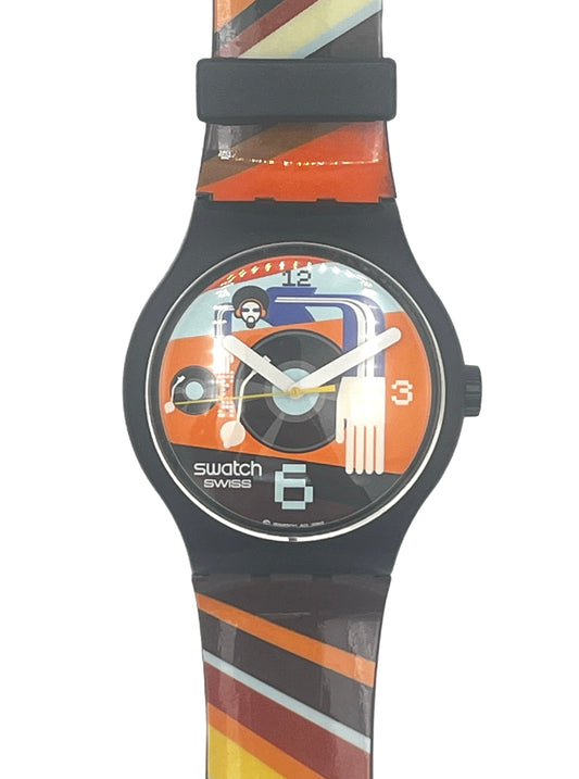 Swatch Swiss wrist watch with a black case and a colorful striped silicone strap featuring orange, yellow, brown, and white diagonal bands. The watch face has a graphic design with a skull, a record player, and the Swatch logo.